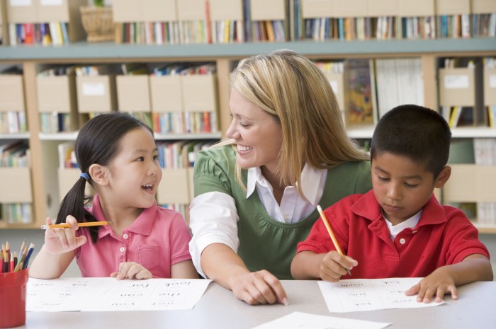 Teacher smiling at two preschool students as they study
