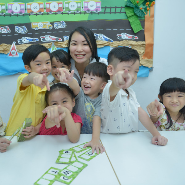 Smiling teacher and children in class pointing at camera